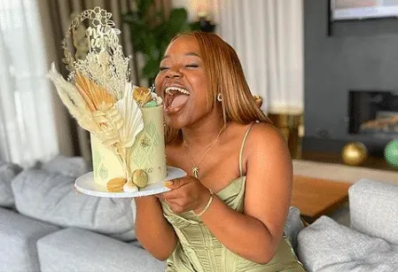 Vee Kativhu pretending to eat an entire cake. She is a beautiful Black woman wearing a pale green dress.