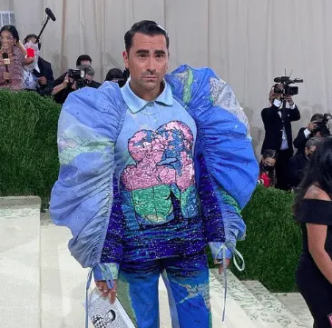 Dan Levy at the 2021 Met Gala wearing a puffy world maps on his sleeves and an image of two men kissing on his chest.