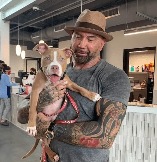 Dave wears a grey t-shirt and a brown hat while holding a smiling Penny the rescue dog.