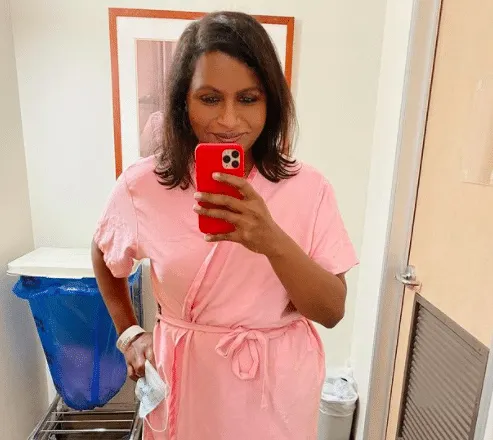 Mindy Kaling wears a pink robe and takes a selfie in a doctor's waiting room