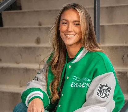 Kylie Kelce wears a green varsity letterman jacket and smiles.