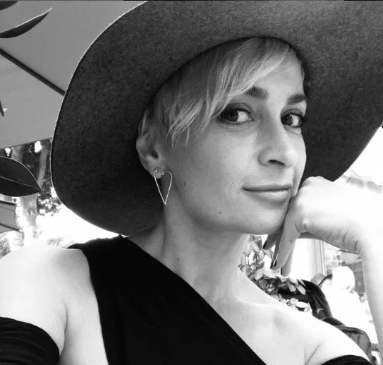 a black and white photo of Halyna Hutchins wearing a hat and smiling