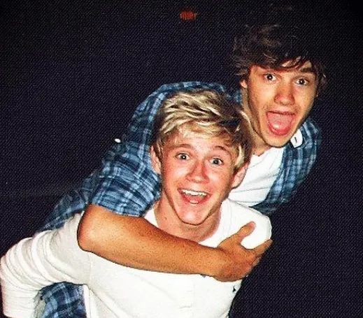 an old photo of Niall Horan and Liam Payne. Liam is jumping on Niall's back and they are both laughing.