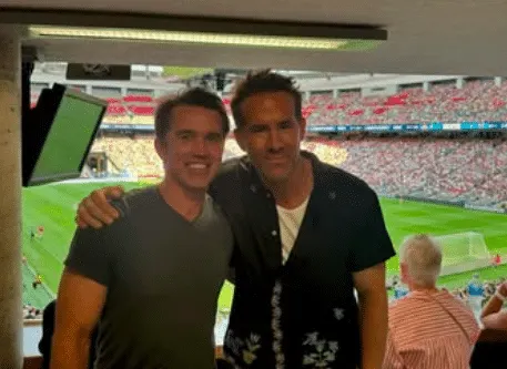 Rob McElhenney and Ryan Reynolds smiling at a Wrexham match.