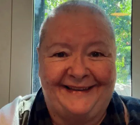 A still of Magda Szubanski with her head shaved. She's smiling as she discusses her cancer diagnosis
