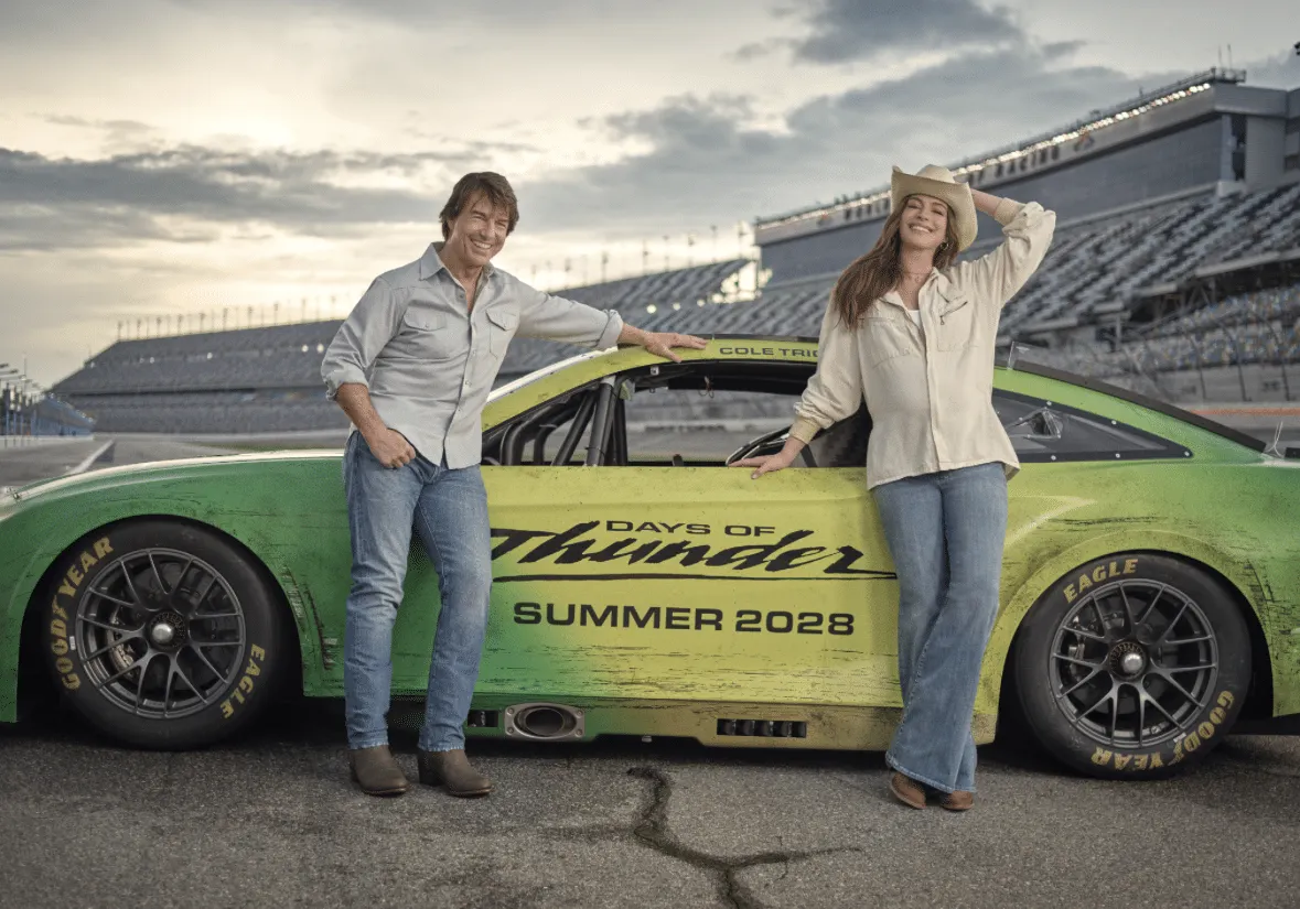 Tom Cruise and Anne Hathaway stand in front of a yellow and green car to announce Days of Thunder sequel