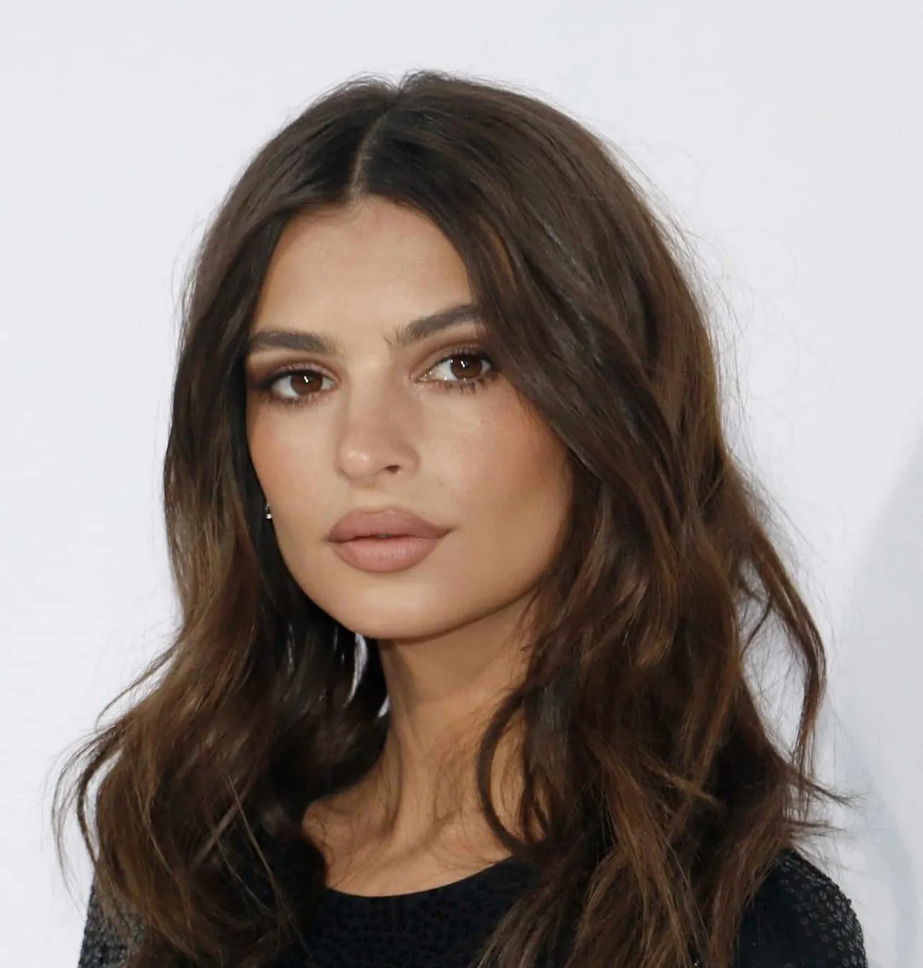 Emily Ratajkowski at a red carpet event. She has long brown hair that sits past her shoulders.