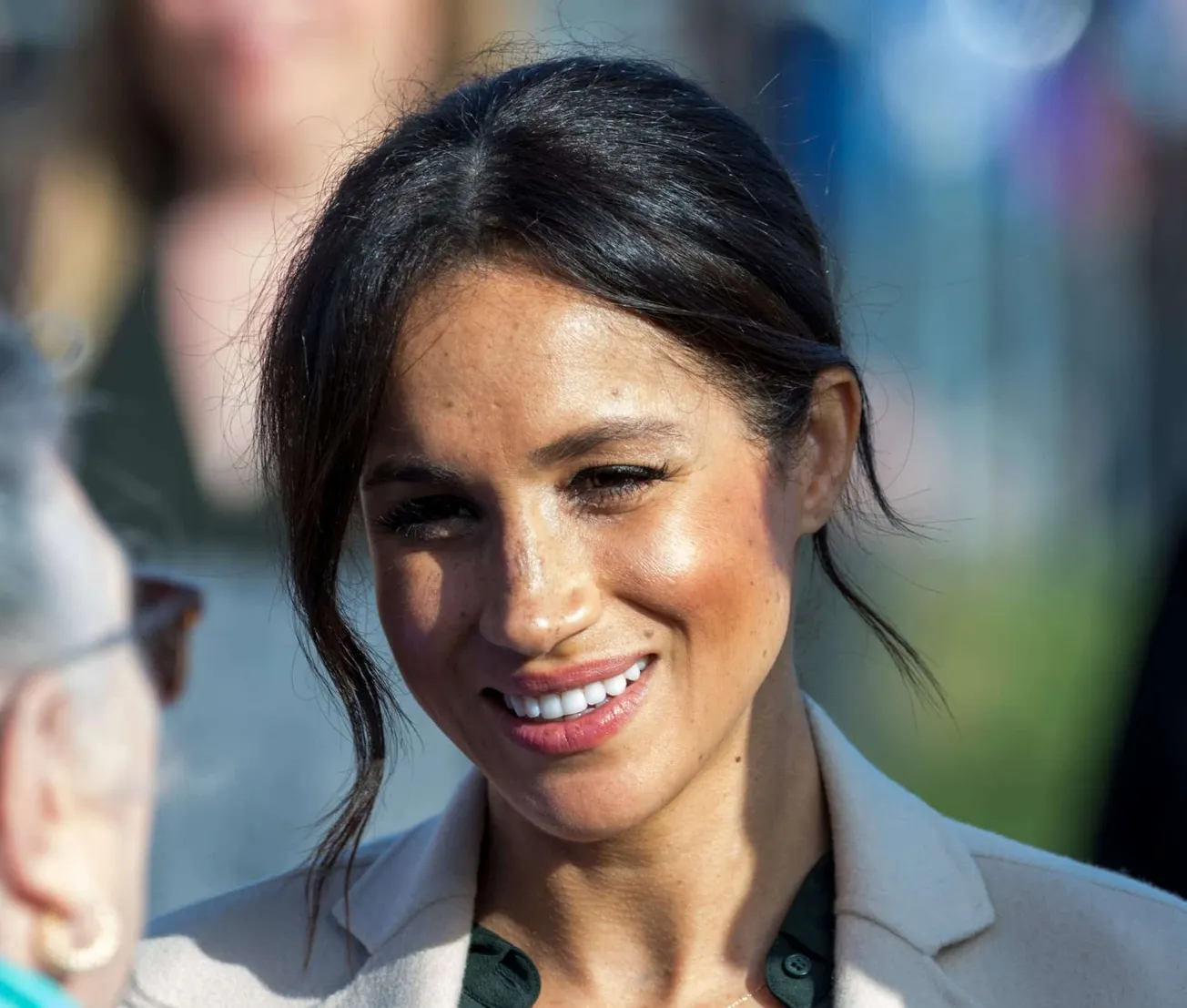A close-up photo of Meghan Markle from the neck up. Her black hair is tied back though a few strands dangle around her face.