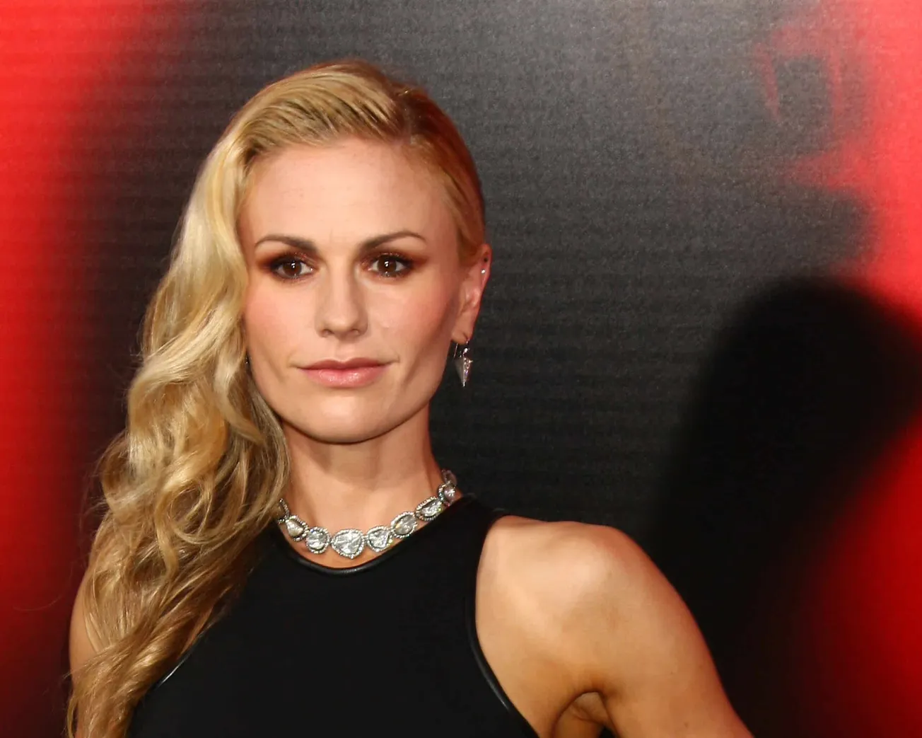 A close up photo of Anna Paquin. She has long blond hair over one shoulder and wears a black, sleevelss gown.