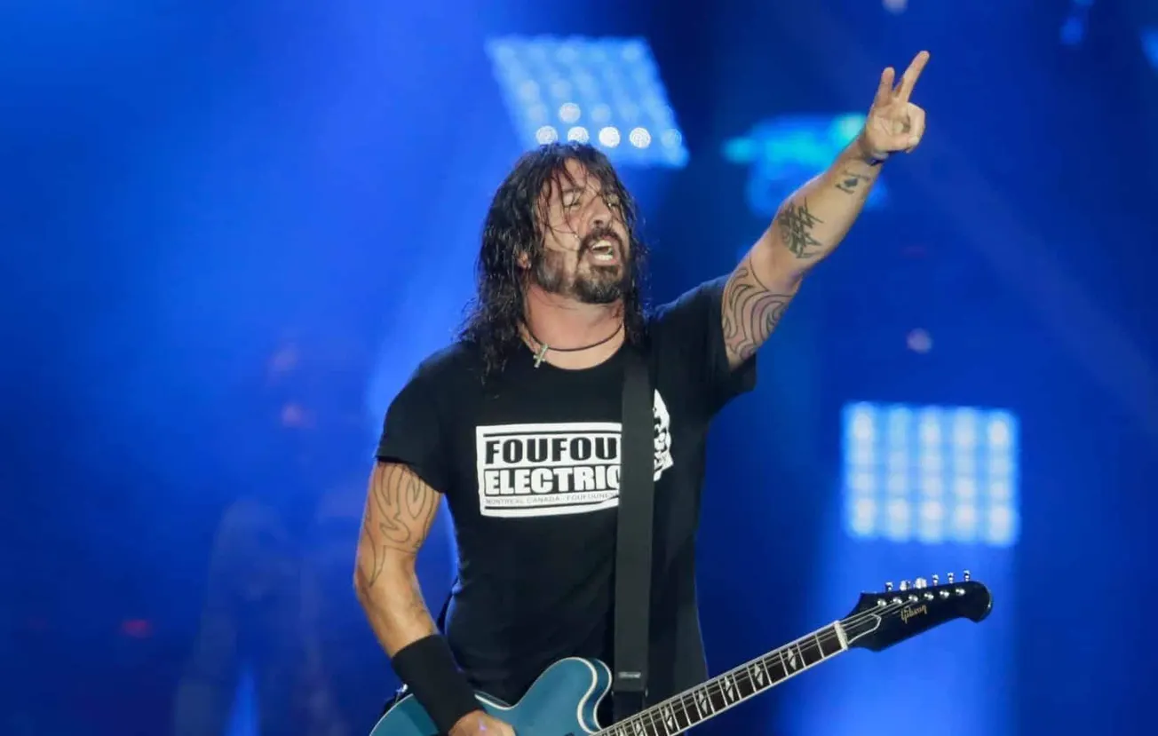 Dave Grohl performs on stage with one hand in the air making a peace sign.