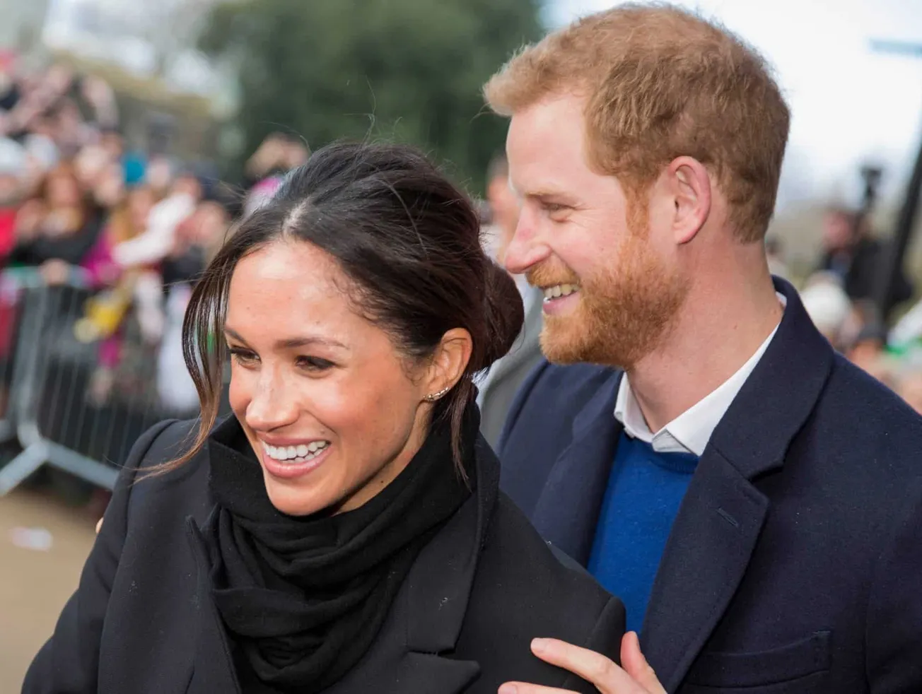 Meghan and Harry smiling together while greeting crowds at a royal event.