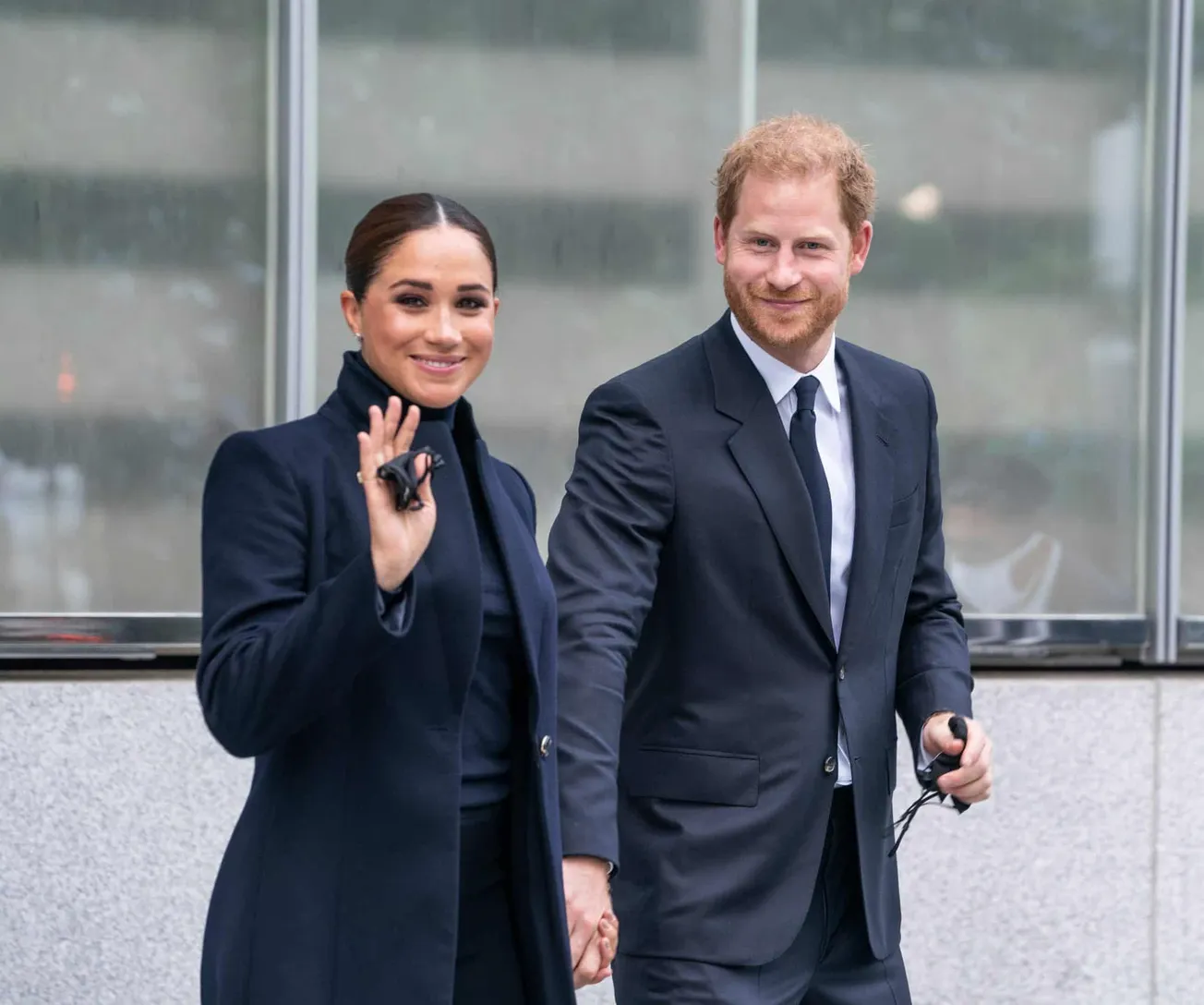 Meghan and Harry dressed in a coat and a suit walking together.