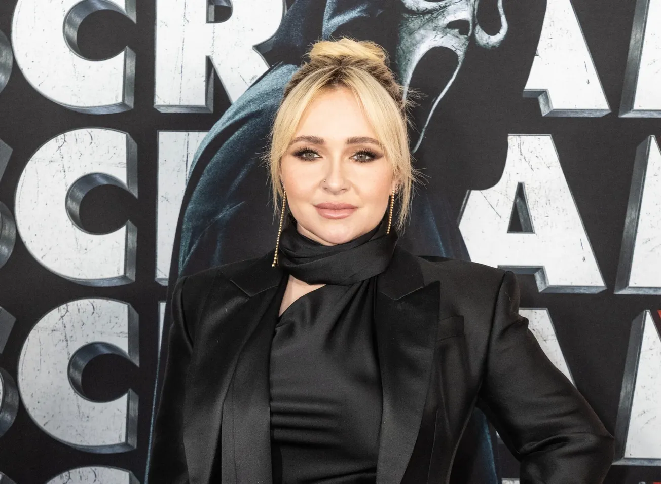 Hayden Panettiere at a press event. She has blonde hair styled up, and wears black.