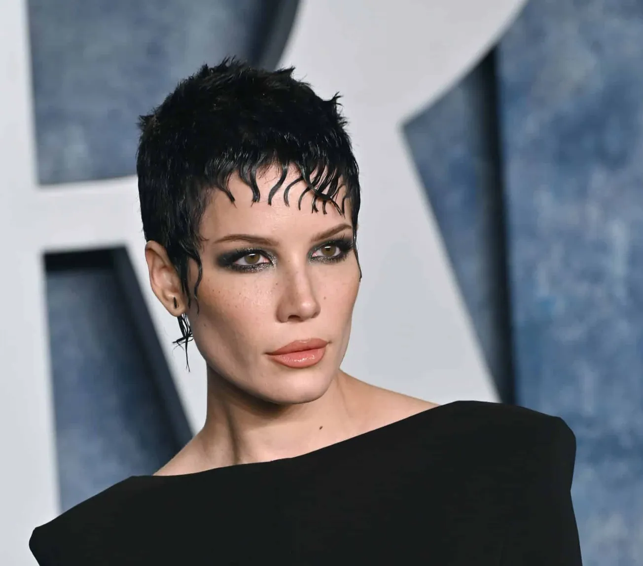 A close up image of Halsey dressed in black with short, styled hair.