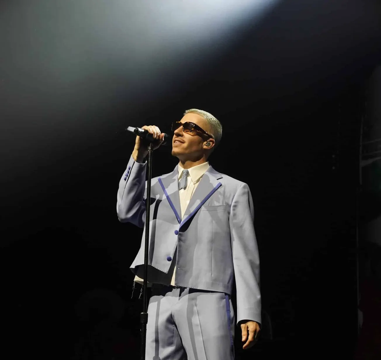 Macklemore performing on stage wearing a grey suit and sunglasses