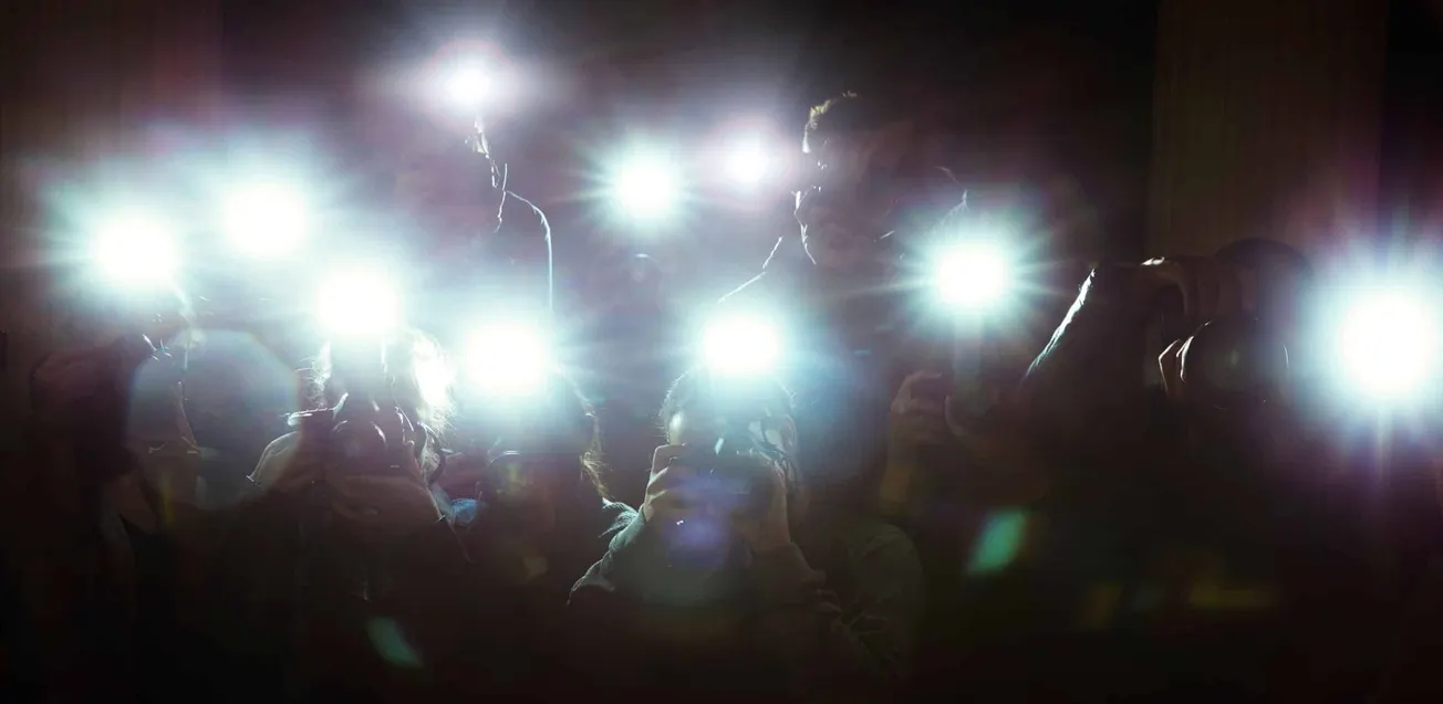 a dark area with paparazzi flash photos going off. Not associated with Harry and Meghan's car chase, just used to illustrate