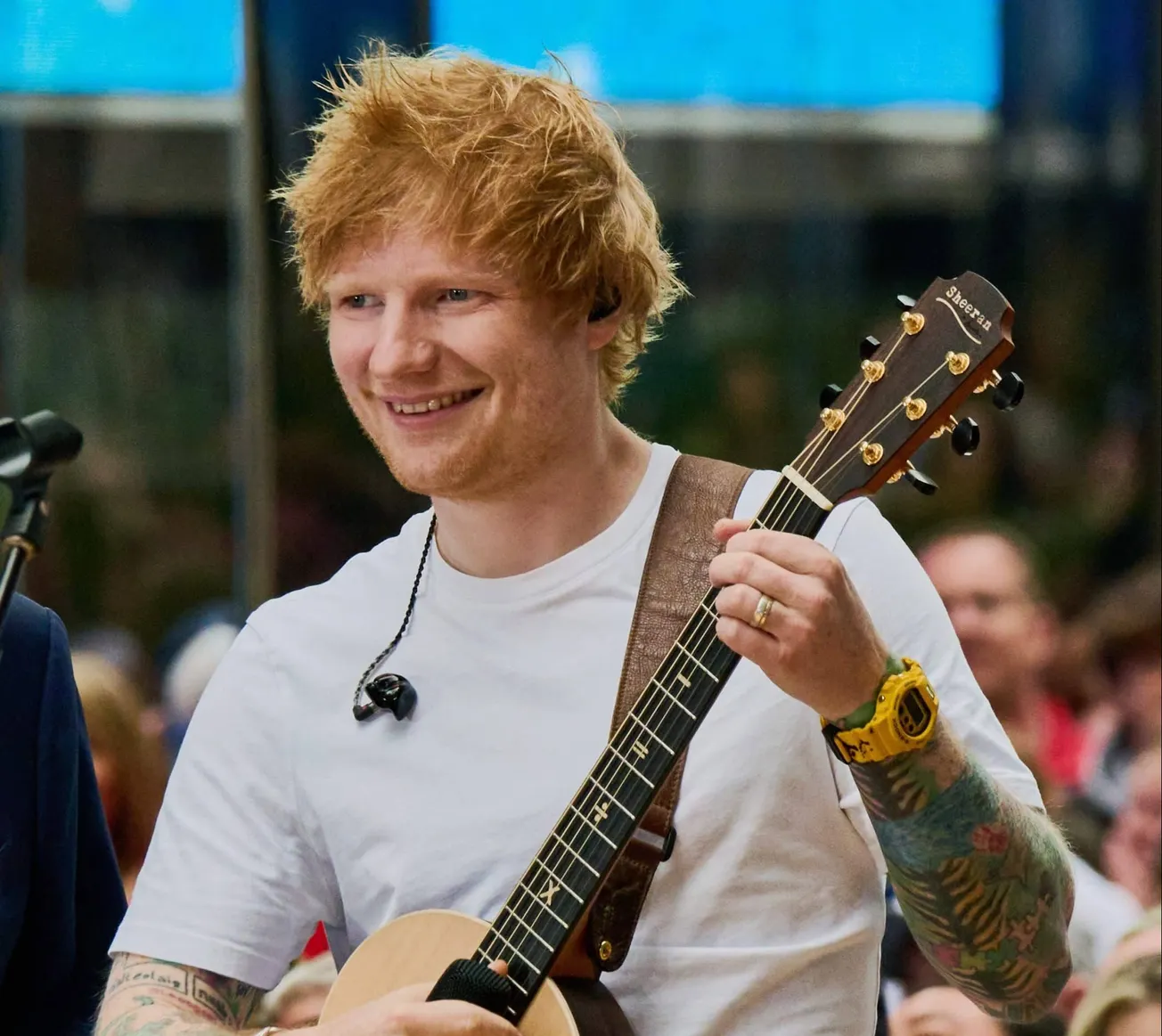 Ed Sheeran holds his guitar and smiles on stage