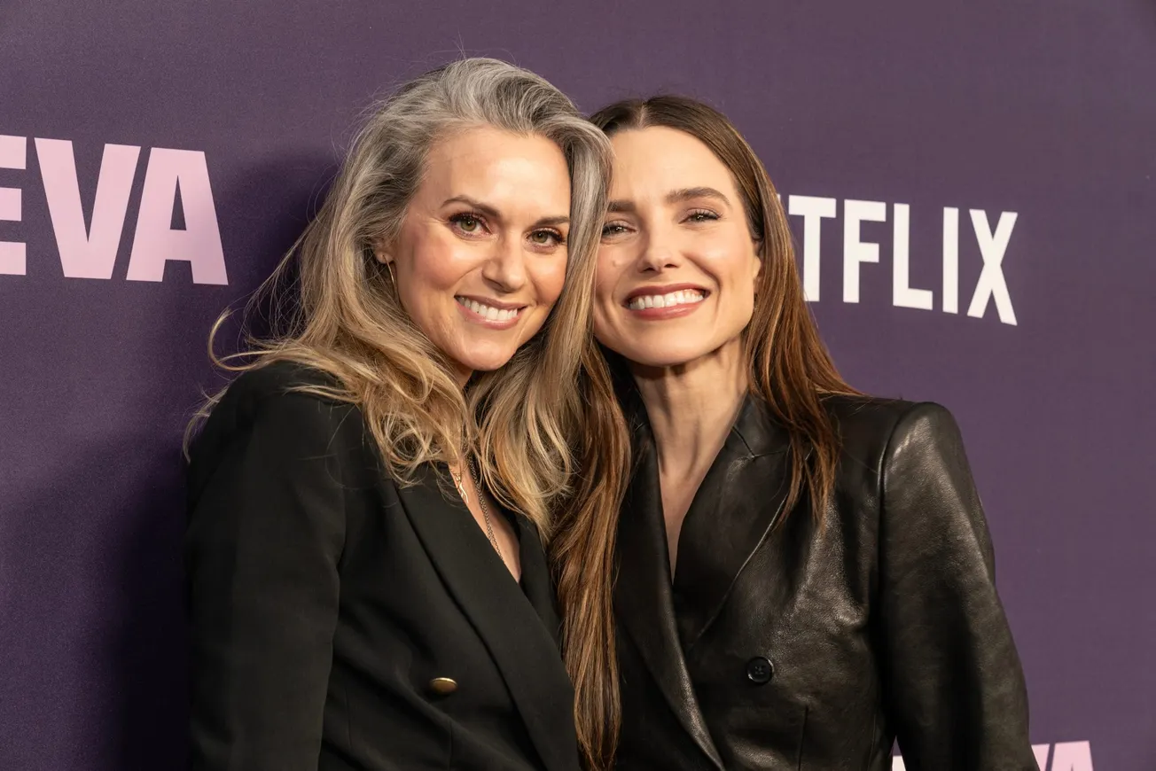 Hilarie Burton and Sophia Bush smile together at a Netflix press event. Their heads lean in towards one another.