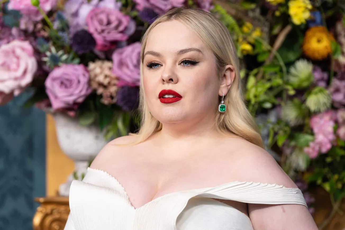close up of Nicola Coughlan at a press event wearig an off-the-shoulder white dress and bright red lipstick.