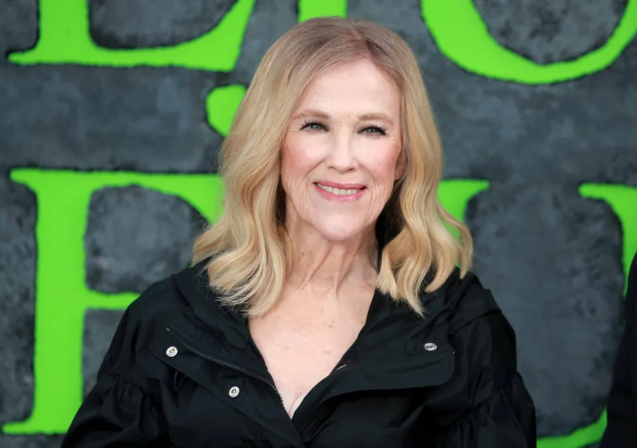 Catherine O'Hara dressed in black and smiling at a red carpet event for Beetlejuice 2.