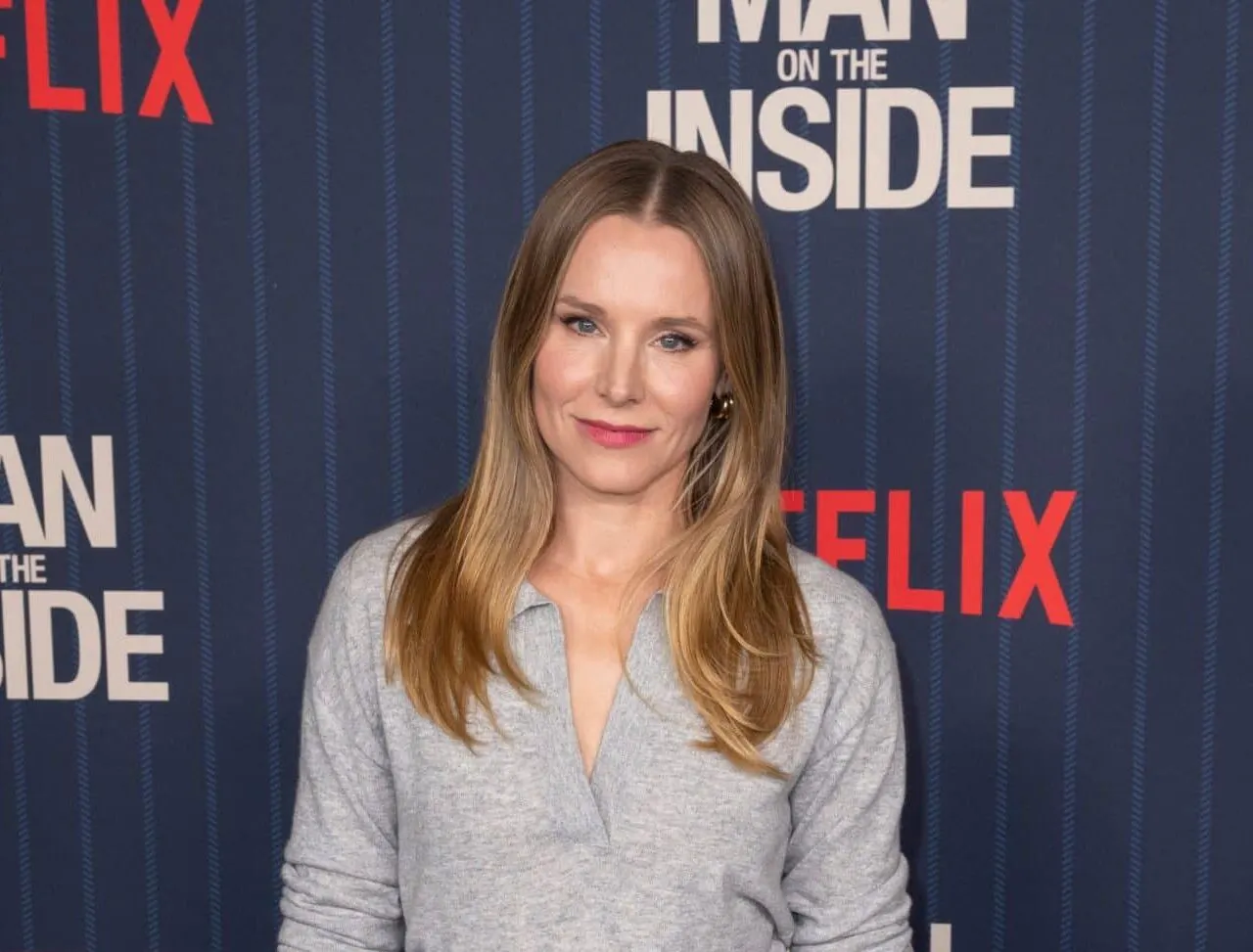 Kristen Bell at the premiere of a Netflix film. SHe wears a grey top and has dark blonde hair that sits over her shoulders.