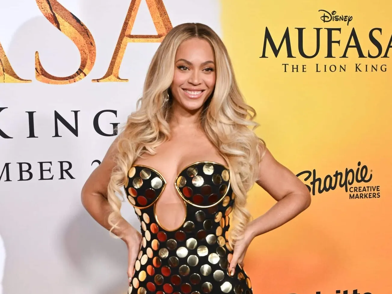 Beyoncé smiles at a red carpet event wearing a gold and black strapless gown. She has long hair down to her waist and has her