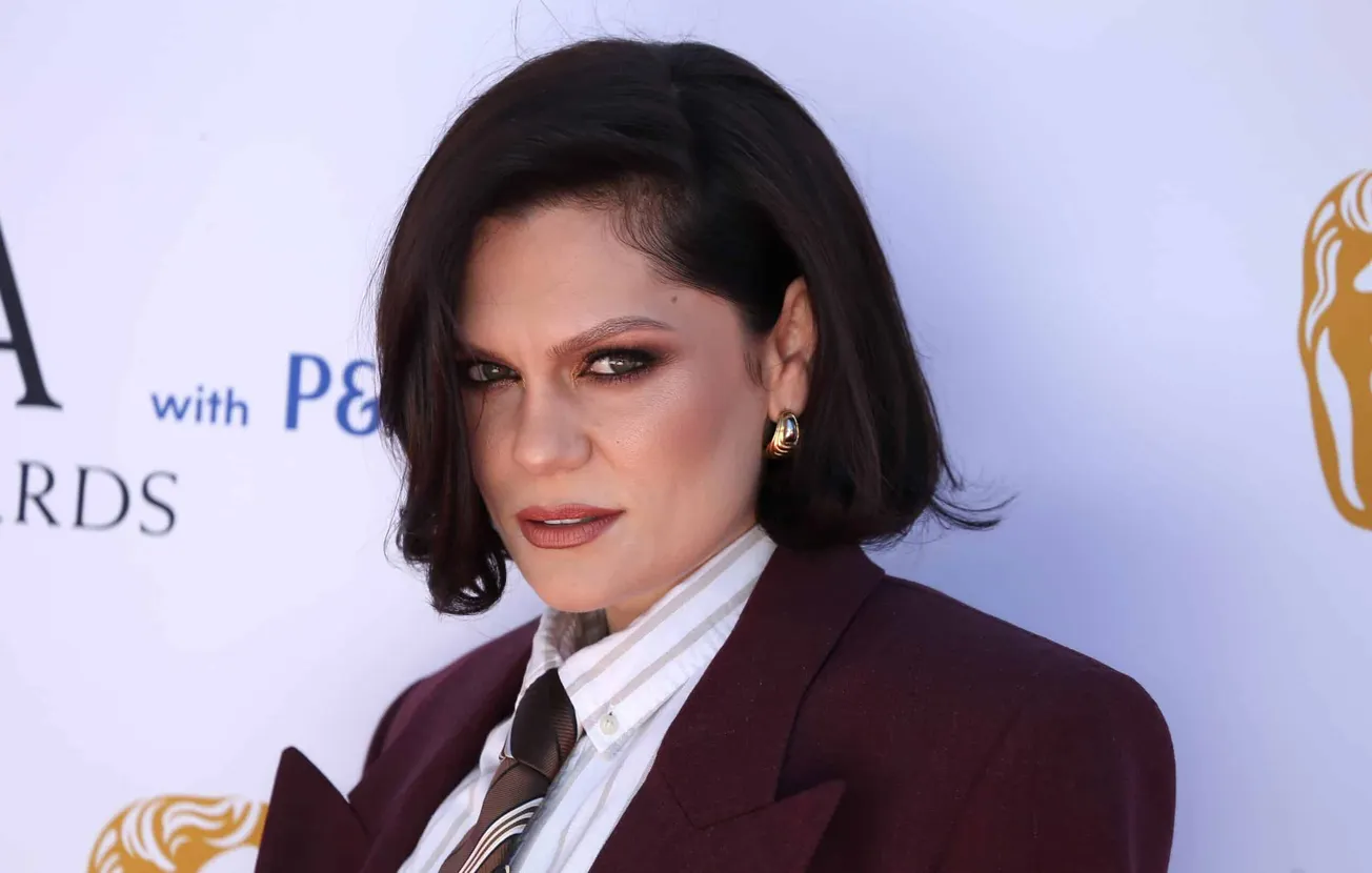 Jessie J at a press event with short black bob hairstyle and wears a suit