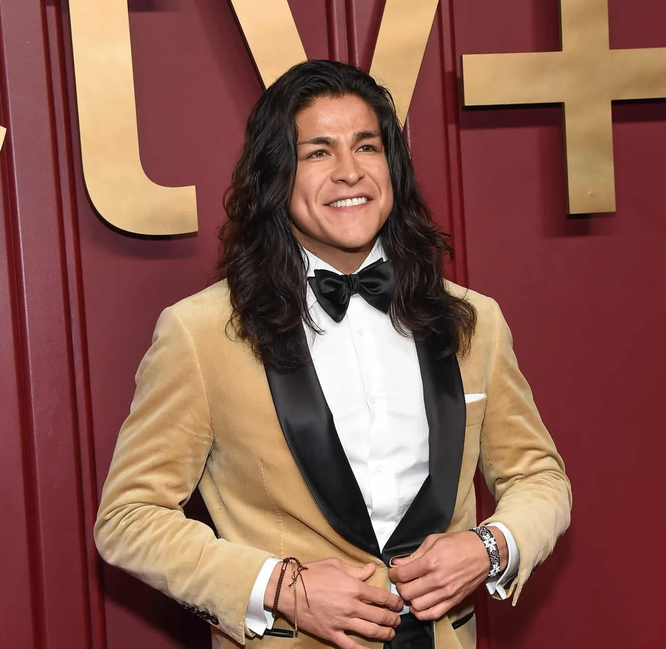 Cristo Fernandez smiles at a press event wearing a gold and black tuxedo