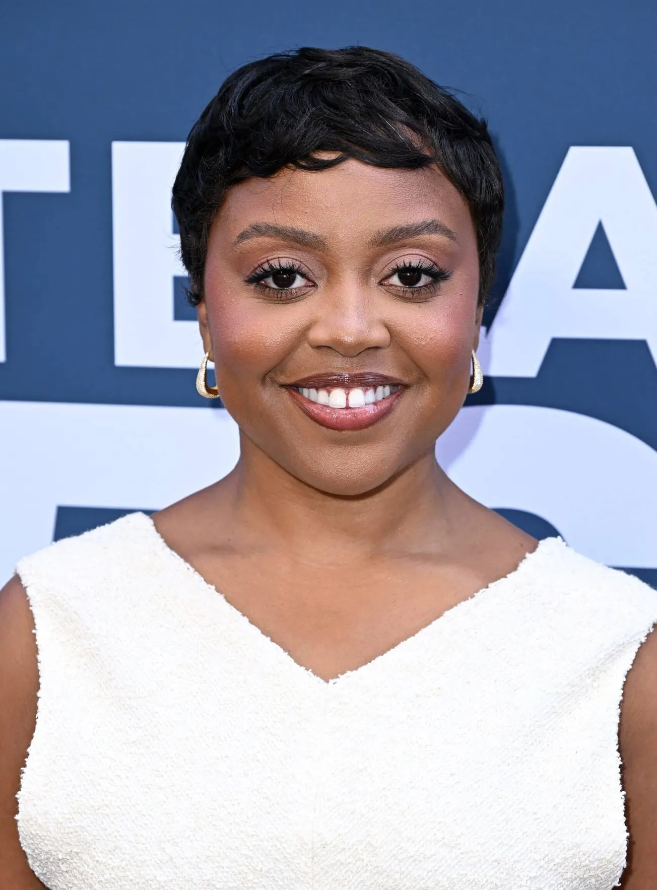 Quinta Brunson dressed in white and smiling at a press event.