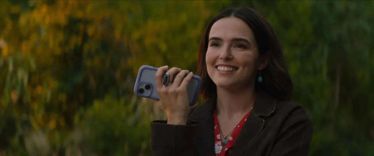 Zoey Deutch as Jill in 'Voicemails for Isabelle'. She's speaking into a phone and smiling.