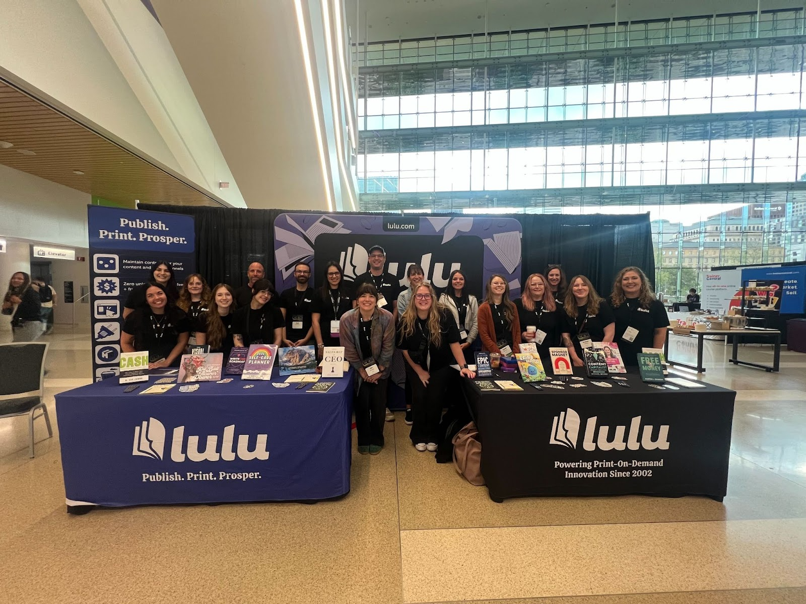 The Lulu Team at CEX - a large group of people behind two tables, scattered with Lulu swag