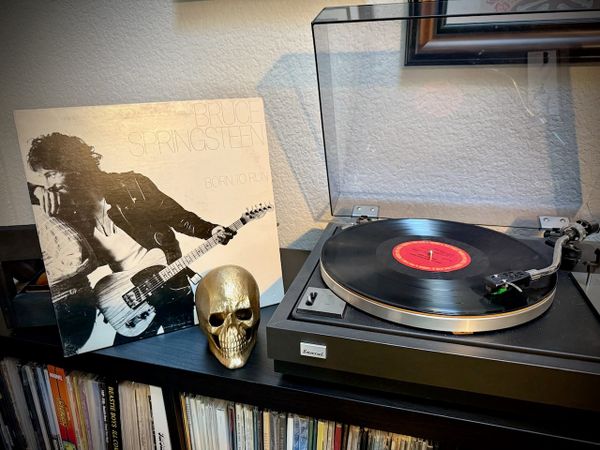 The album jacket for Born to Run by Bruce Springsteen propped up next to a record player, which is playing the album.
