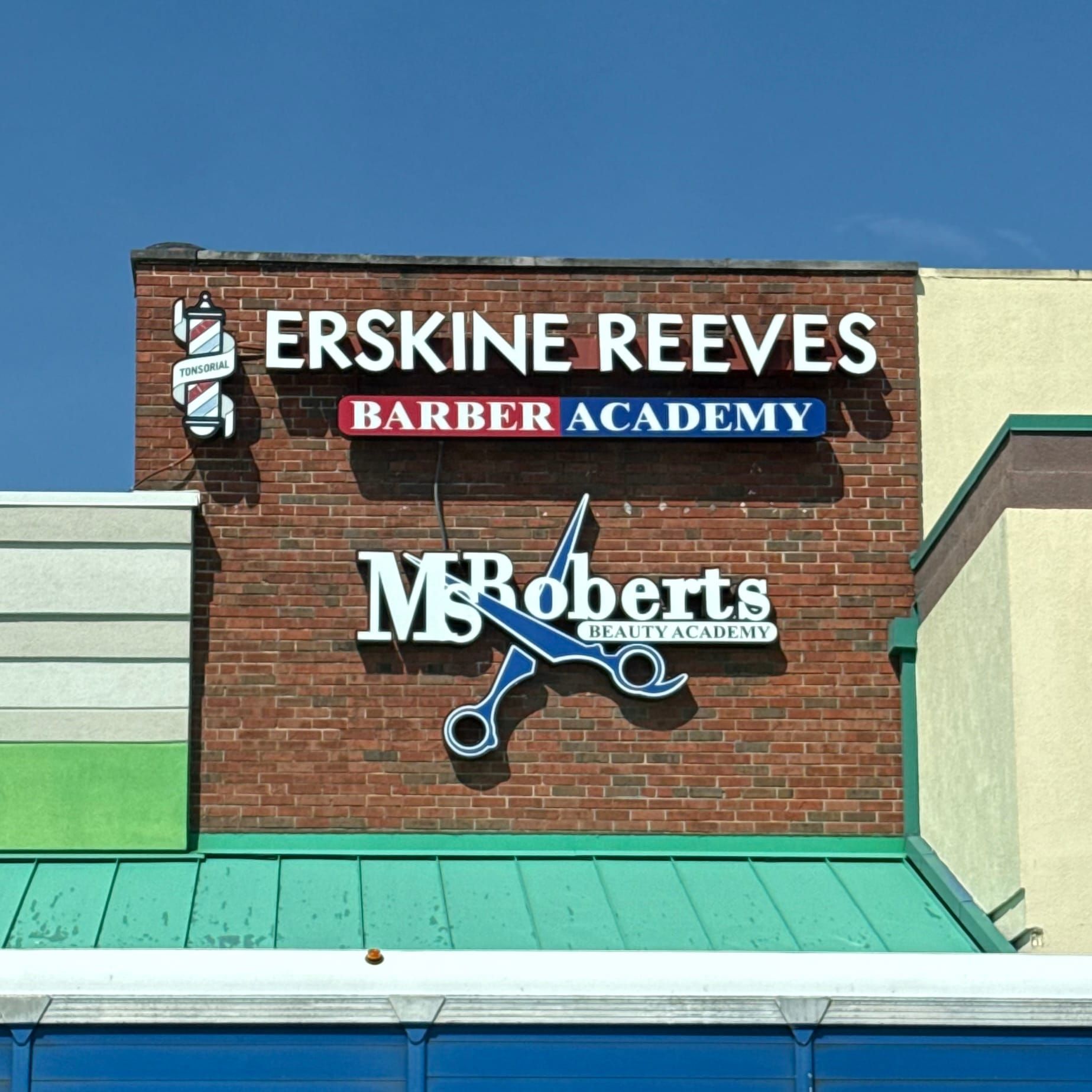 A brick shopping center fascia with a sign for Erskine Reeves Barber Academy and Ms Roberts Beauty Academy