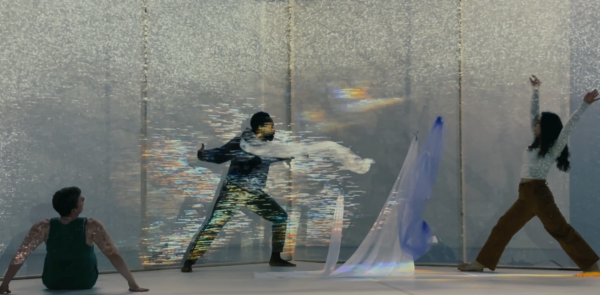 Three dancers on stage against a wall of noise, mid-pose on stage engaging with floating fabrics.