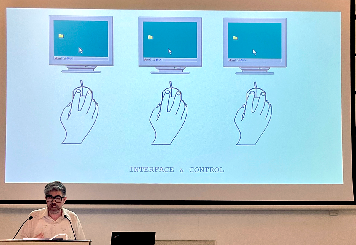Bearded man with gray hair and glasses in front of a projection of 90s era gifs: three hands holding mouse devices connected to computer screens.