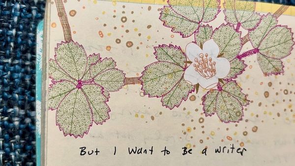 Page from a notebook with green leaves and a white flower printed on the page. Text in sloppy blank ink says: "But I want to Be a writer"