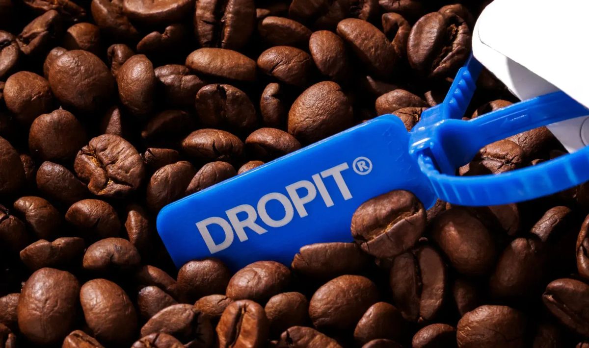 Embalagem de café branca, com um lacre azul escrito DROPIT, sobre vários grãos de café torrados