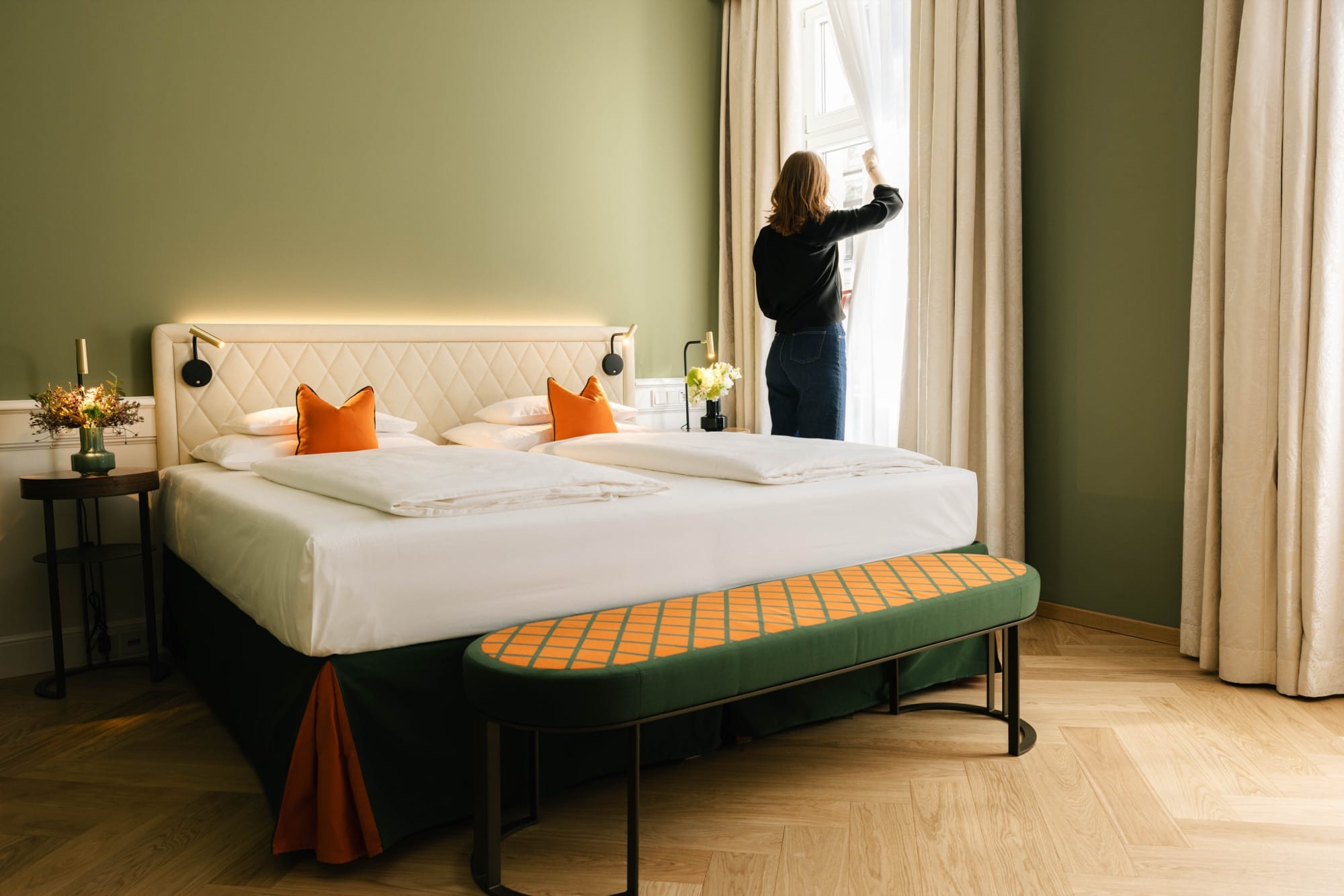 Mitarbeiterin richtet die Vorhänge in einem Hotelzimmer mit grünen Wänden und Doppelbett