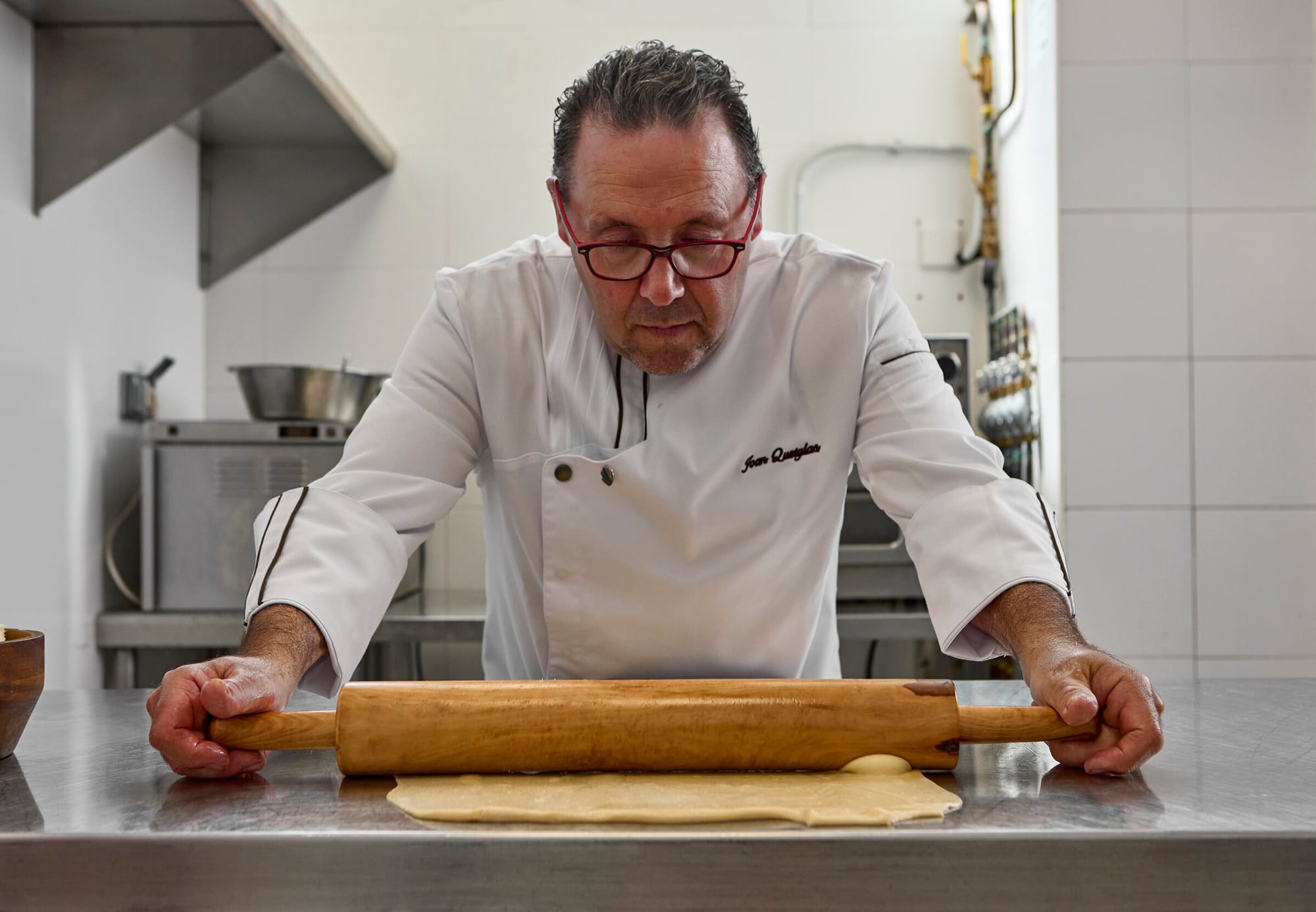 Juan Quetglas Lopez in weißer Kochjacke rollt mit einem Holznudelholz Teig auf einer Edelstahlarbeitsfläche aus