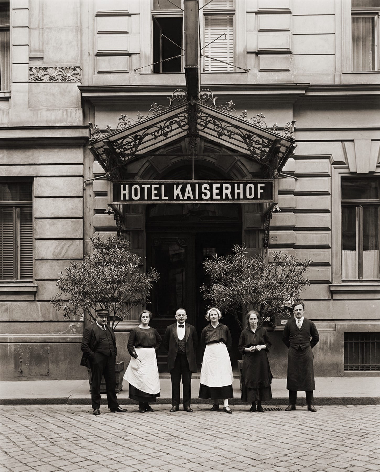 Historische Schwarz-Weiß-Aufnahme: sechs Mitarbeiterinnen und Mitarbeiter vor dem Eingang mit dem Schriftzug HOTEL KAISERHOF