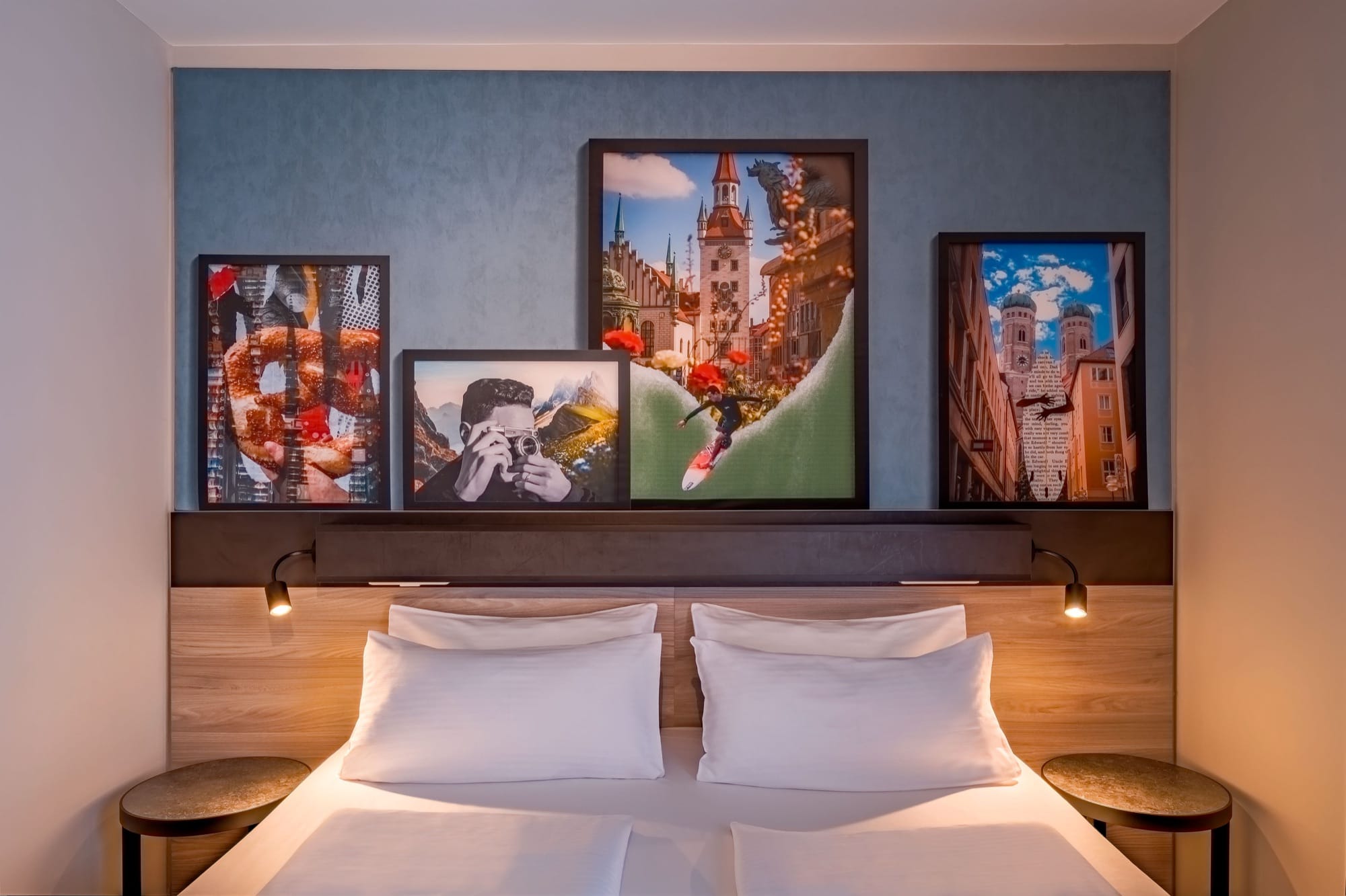 Doppelbett mit weißer Bettwäsche vor einer blauen Wand mit vier gerahmten Collagen von Münchner Sehenswürdigkeiten
