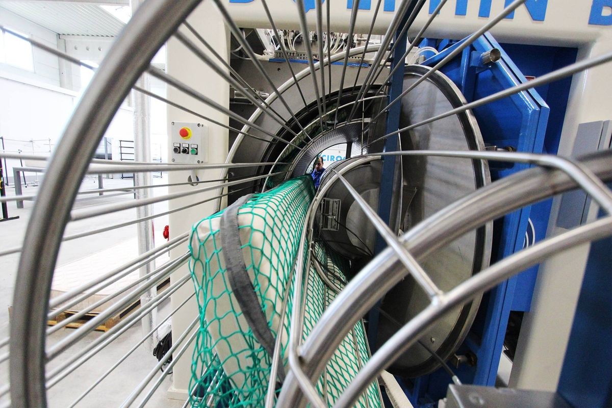 Eine in ein grünes Netz gespannte Matratze wird in die Trommel einer großen industriellen Waschanlage eingeführt