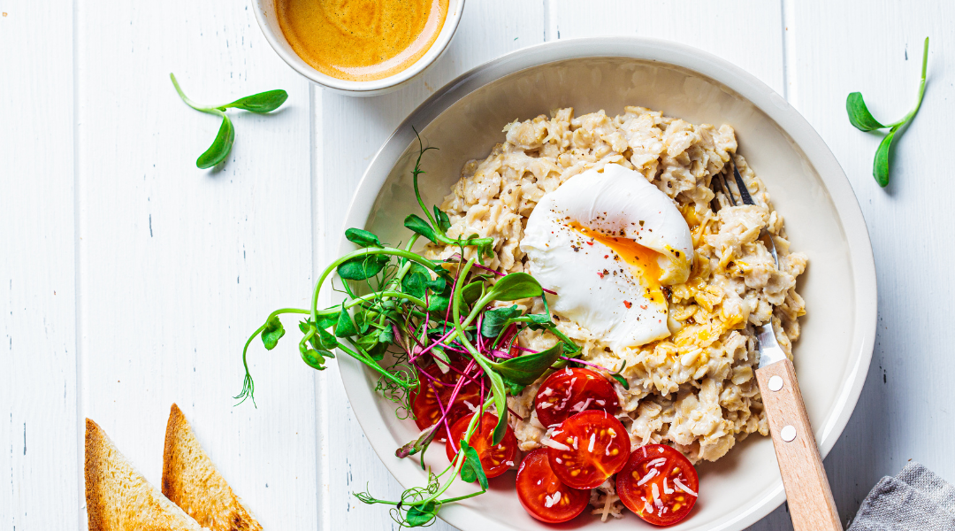 Savory oatmeal with poached egg, tomatoes, cheese and sprouts in white bowl. Healthy breakfast concept.
