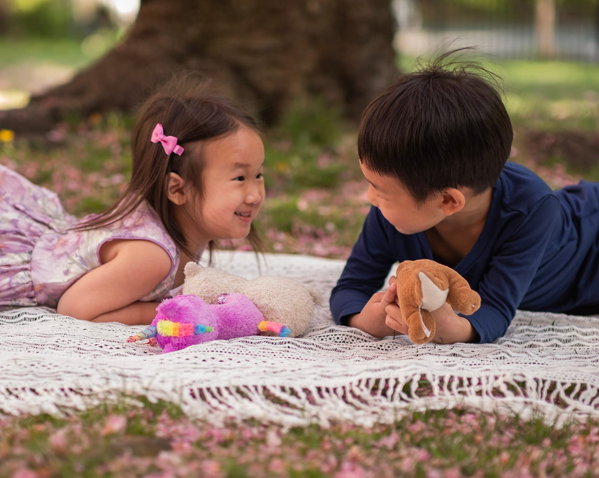 Kids laying on a white blanket and smiling at each other with spring flower petals all around