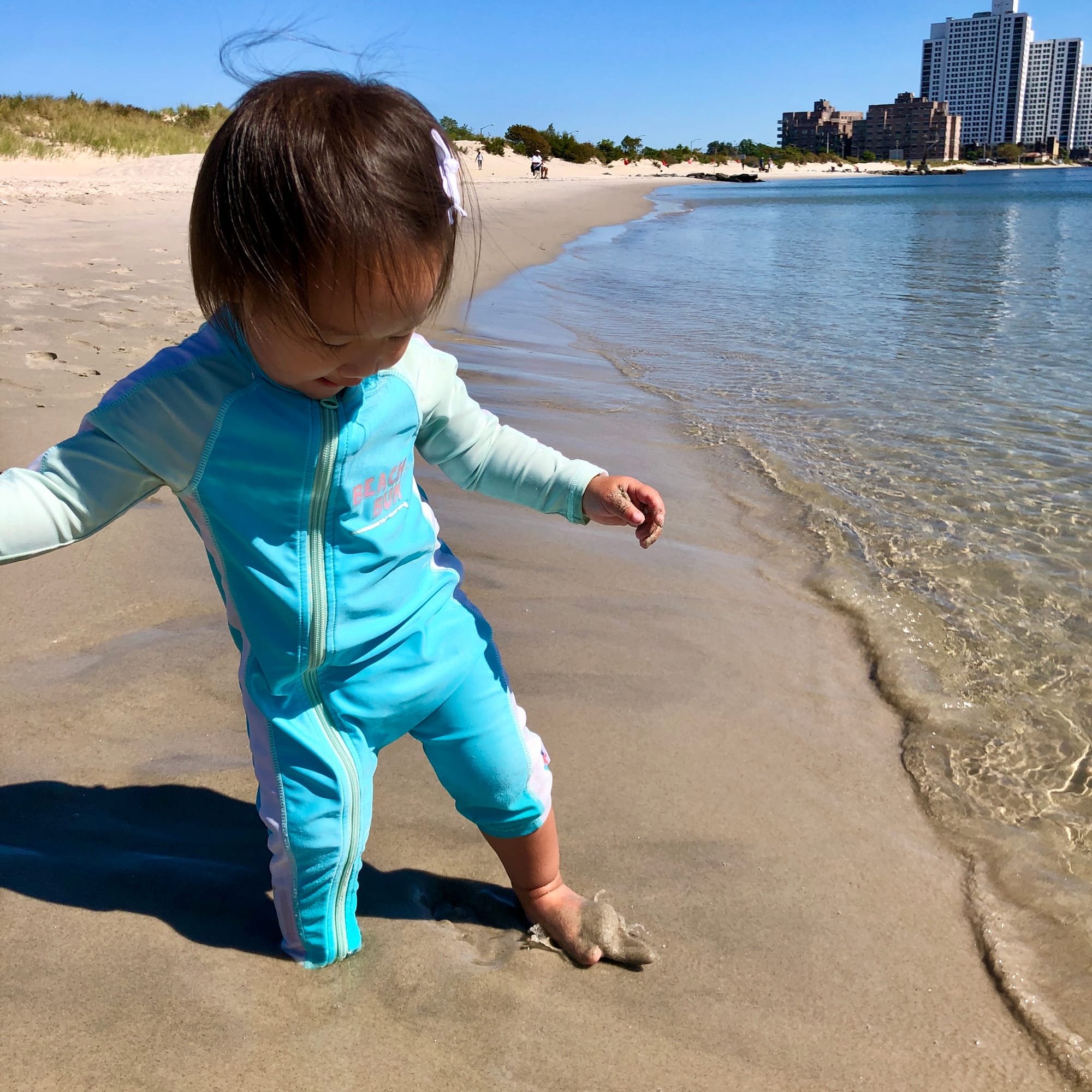 Toddler girl in zip up sun suit playing along the shore