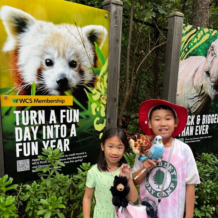 Kids with stuffed animals standing in front of a WCS Membership poster with a red panda that says turn a fun day into a fun year