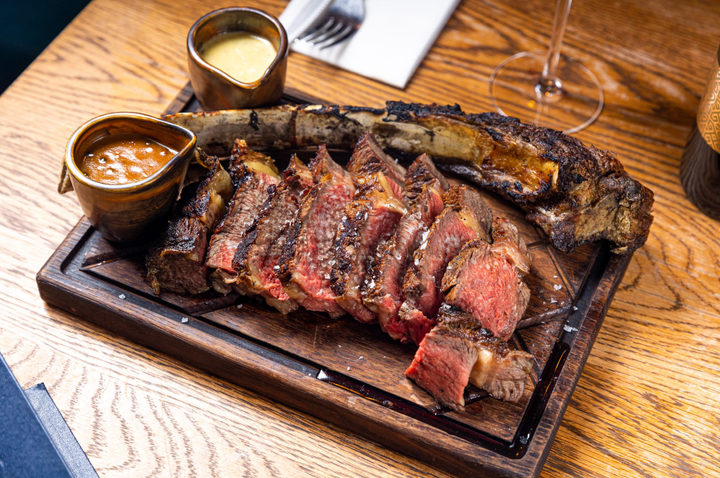 A wooden board containing steak and two dipping sauces