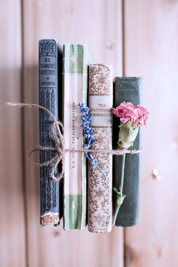 Four aged books, spines facing the viewer, and two flowers tied together with twine.