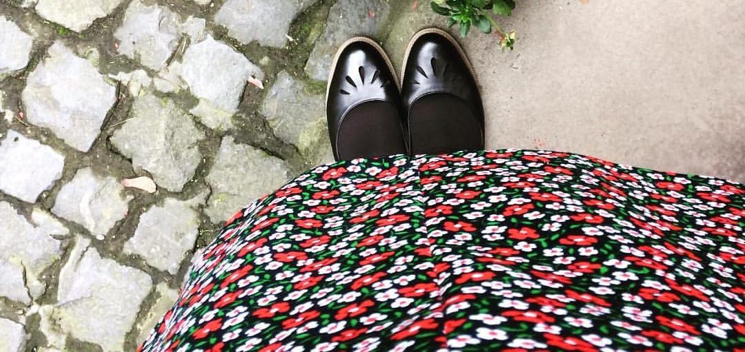 A picture of a pair of feet in black shoes beneath a red and white flowered dress