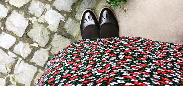 A picture of a pair of feet in black shoes beneath a red and white flowered dress